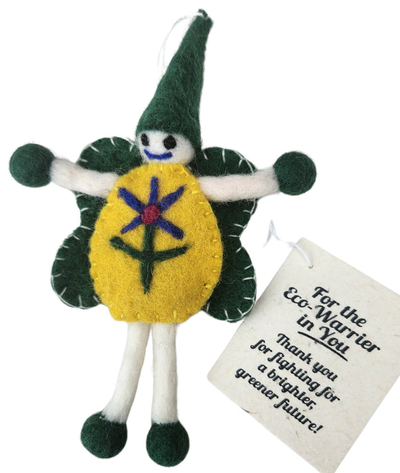 A handmade felt flower doll ornament with a yellow body, green pointed hat and wings, white limbs, and a hanging tag that reads 'For the Eco-Warrior in You'.