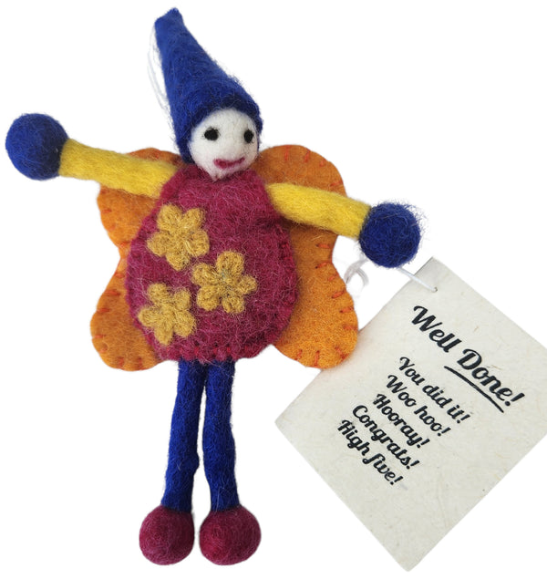 Handmade felted wool doll with a blue hat, yellow arms, orange wings, and a magenta dress with yellow flowers, shown with a 'Well Done!' paper tag on a white background.