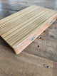 A closed, folding wooden backgammon set, featuring small metal latch closures, resting on a rustic wooden surface.