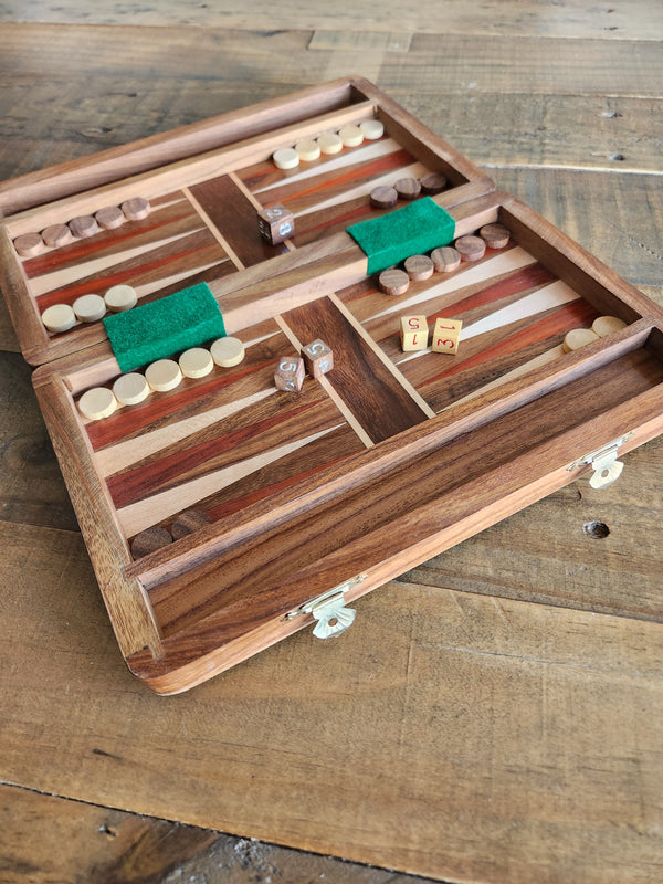 An open wooden backgammon board set with inlaid wooden playing surface, green felt, doubles block, checkers, and dice, placed on a rustic wooden tabletop.