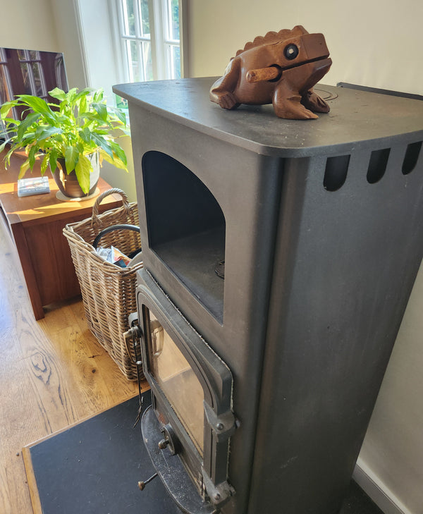 Wood-burning stove with a decorative frog on top in a room with table and plant.