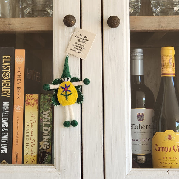 A handmade green and yellow wool felt fairy/pixie ornament hangs from a white cabinet door in a home setting