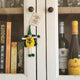 A handmade green and yellow wool felt fairy/pixie ornament hangs from a white cabinet door in a home setting