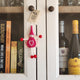 A small pink felt fairy/pixie keepsake with a white heart on its belly, hanging on a white wooden cabinet door.