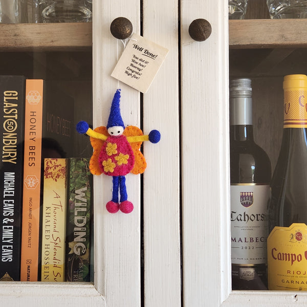 A felt fairy/pixie keepsake hanging from a cupboard door. The 'Well Done' gift tag is shown.