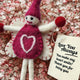 A handmade felt fairy/pixie gift tag/keepsake in pink, displayed on a bed of pink and white flower petals next to a cream paper tag that reads 'Love You Always'.