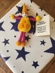 A handmade felt birthday message tag featuring a colorful fairy with yellow, pink, and purple details, placed on top of a white gift box decorated with navy blue stars. A small gift tag next to the doll reads 'Happy Birthday!'.