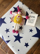 A handmade felt gift tag featuring a small whimsical fairy keepsake with pink and yellow colours, placed on top of a white gift box decorated with navy blue stars. A small tag next to it reads 'Thinking of You'.