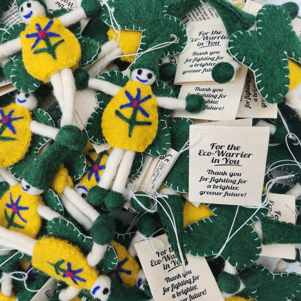 A pile of handmade felt flower fairies in green and yellow with embroidered faces and stems, attached to white tags that read 'For the Eco-Warrior in You. Thank you for fighting for a brighter greener future!'.