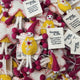 A pile of handmade felt fairy/pixie keepsakes/gift tags, each with a white tag that reads 'Thinking of You'. The ornaments feature yellow felt dresses, pink felt hats and pom-poms, and white felt bodies and legs.