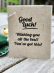 A handmade gift tag made from natural beige paper with black printed text reading 'Good Luck! Wishing you all the best! You've got this!'