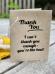 A handmade paper Thank you message with black printed text reading 'Thank You. I can't thank you enough - you're the best!' resting on a weathered wooden surface.